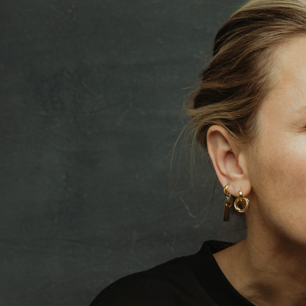 Close-up of a person wearing gold hoop earrings against a dark background
