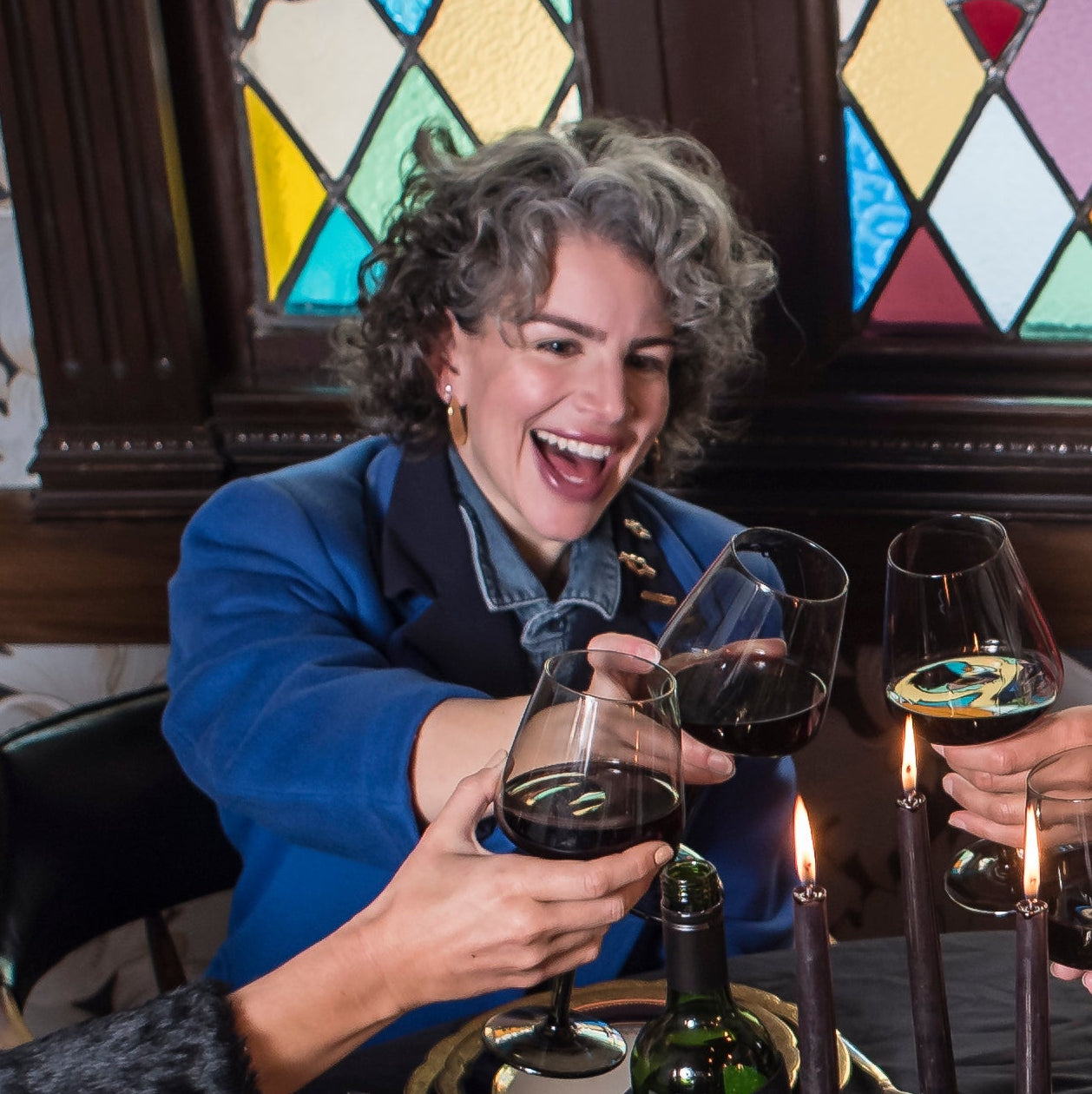 Woman in a blue jacket holding a glass of red wine in front of a stained glass window