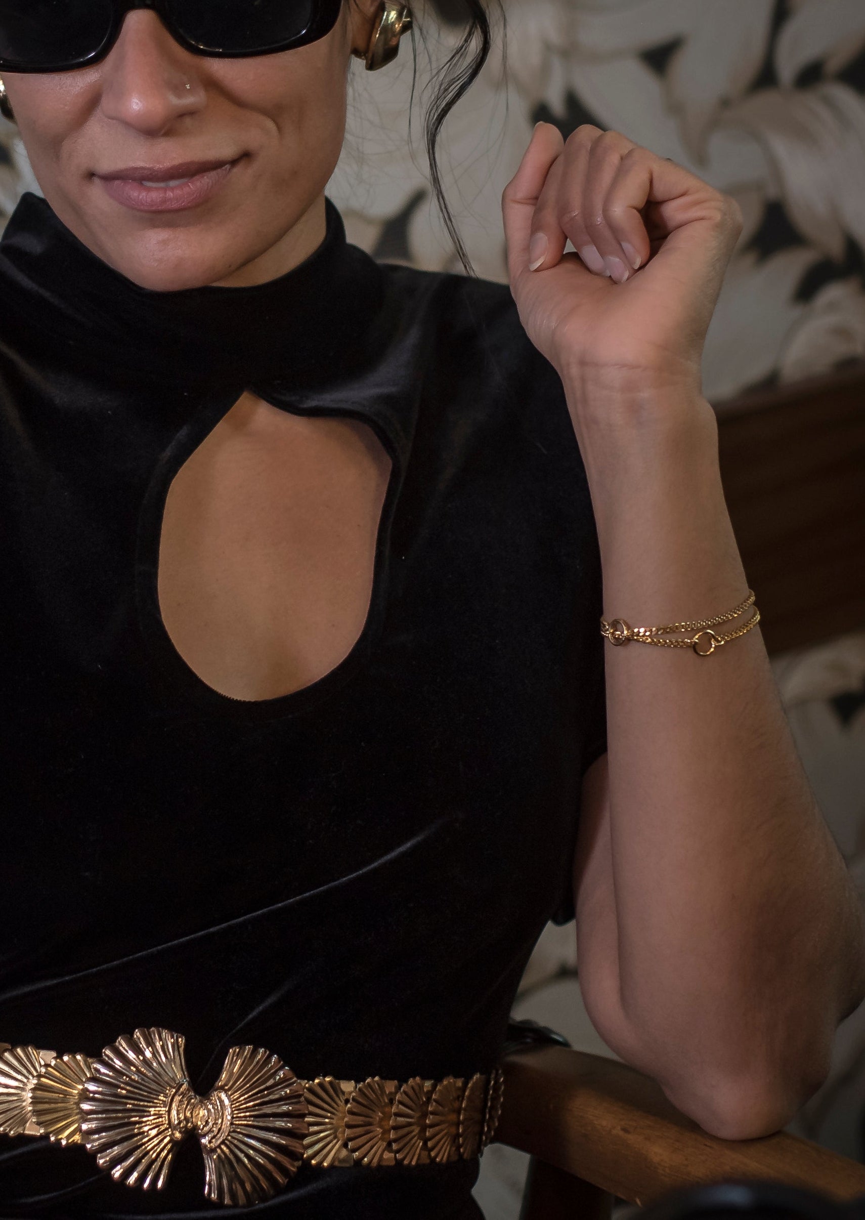 Woman in a black dress with a gold belt sitting indoors.