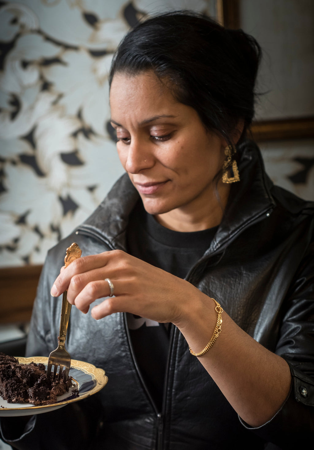 Woman in a leather jacket eating a piece of cake in a cozy setting.