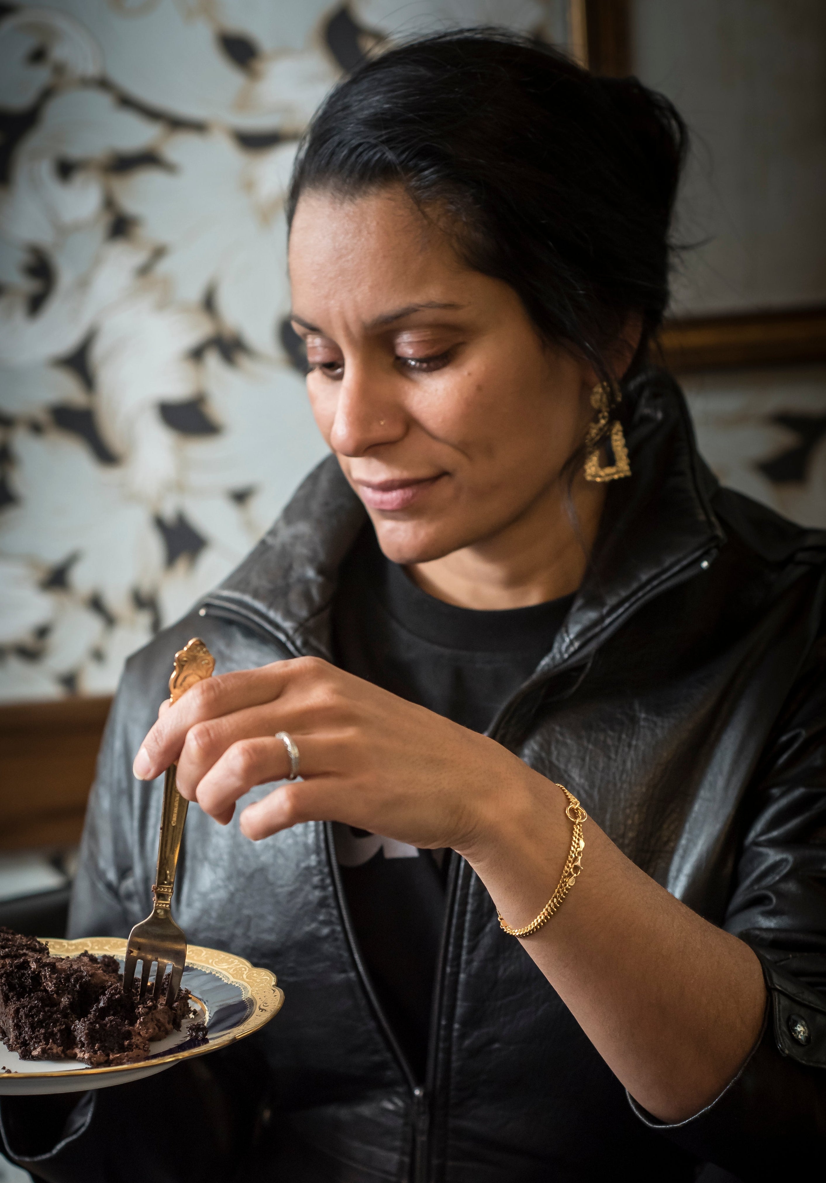 Woman in a leather jacket eating a piece of cake in a cozy setting.