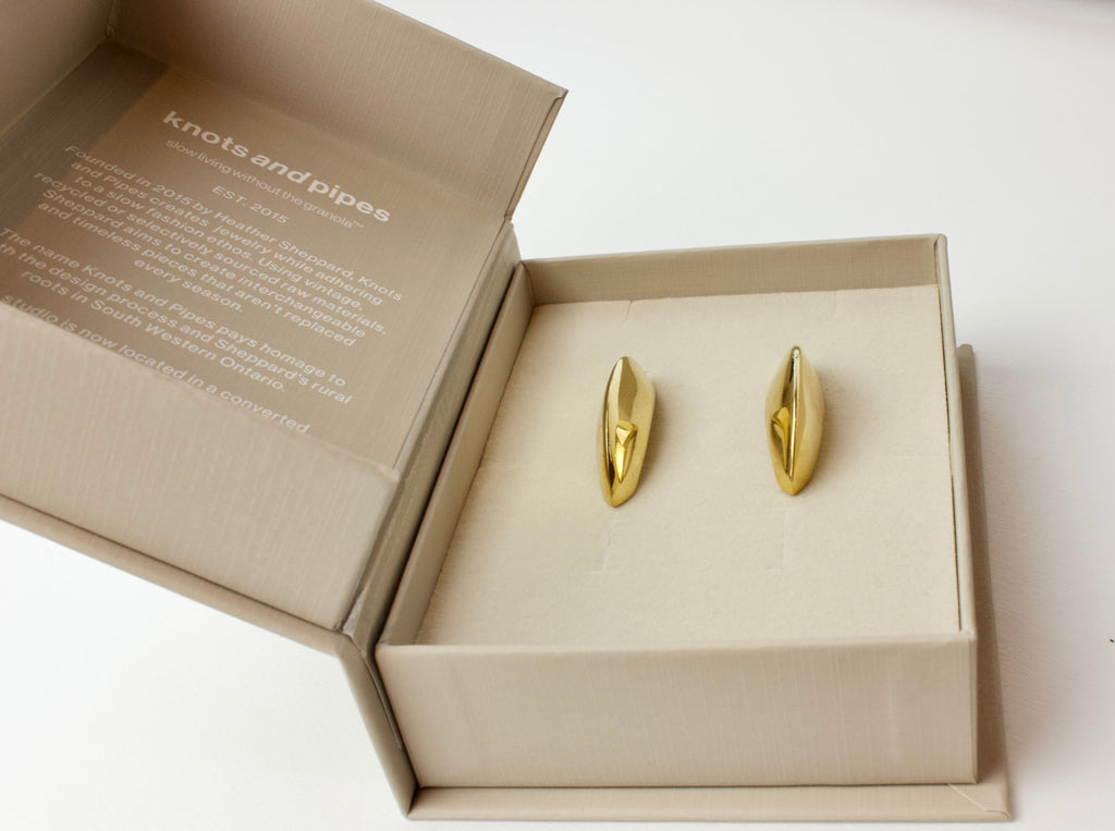 Gold earrings in a 'knotsandpipes' box on a white background