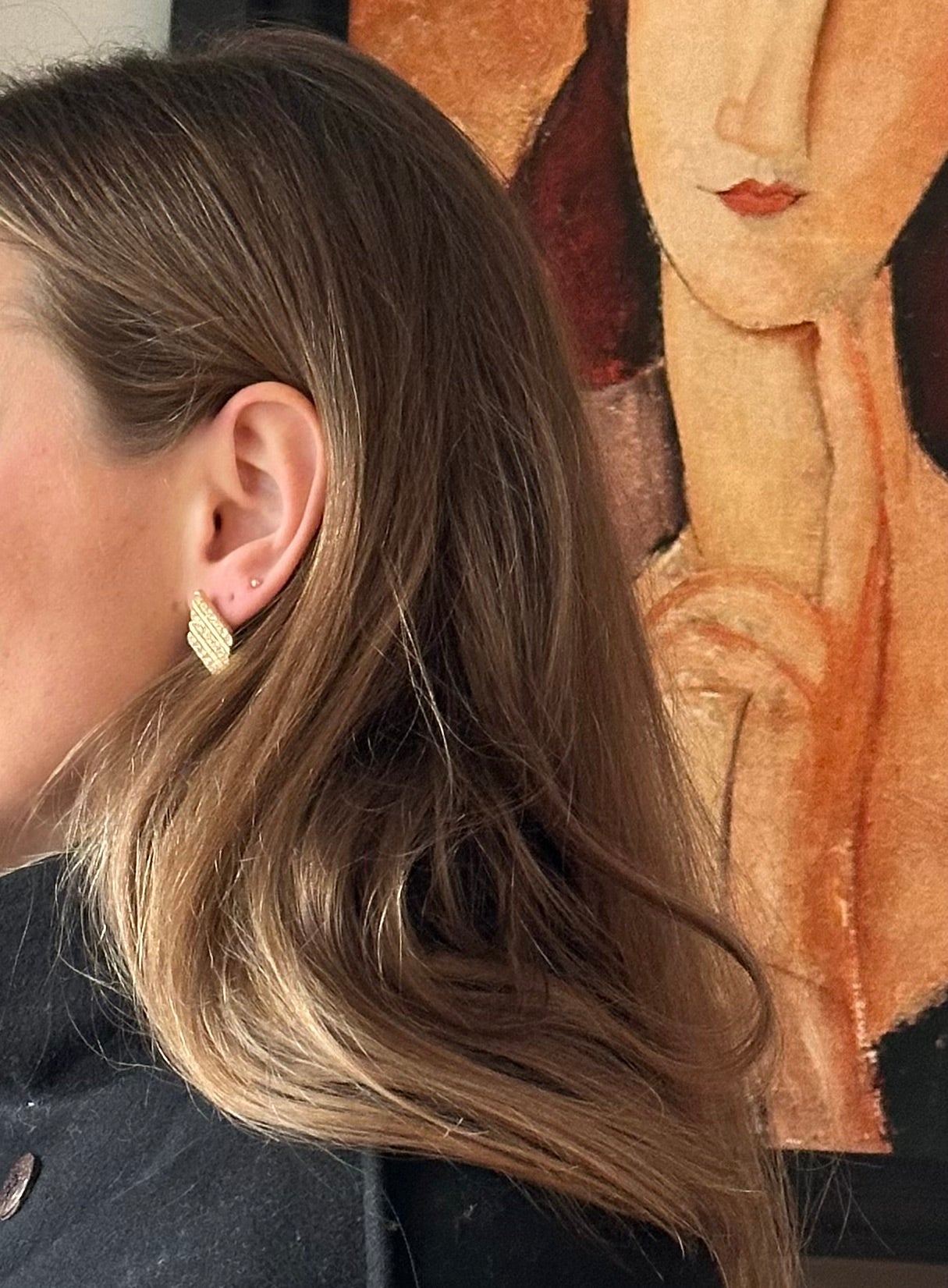Close-up of a person wearing gold earrings with a classical painting in the background