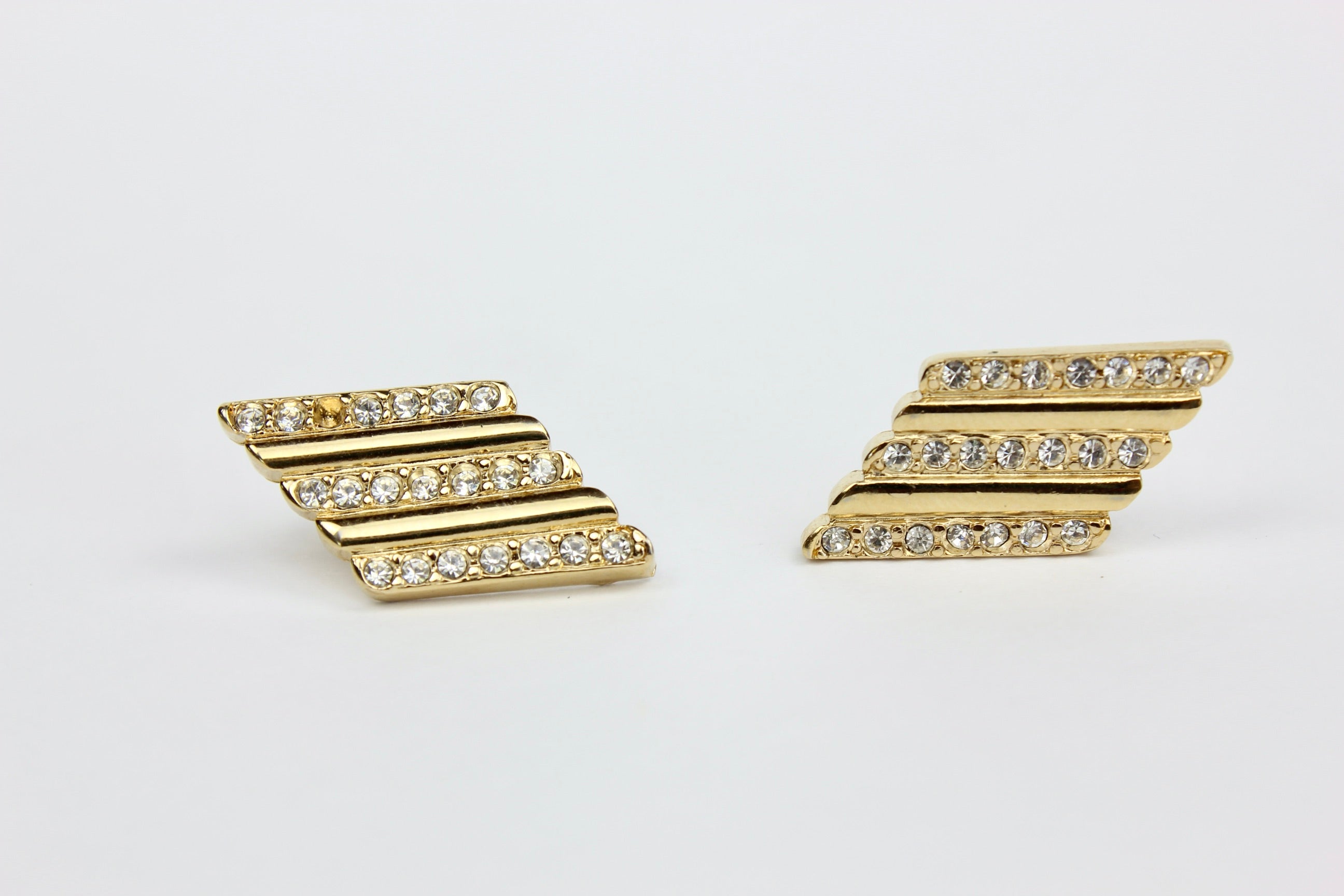 Gold chevron-shaped earrings with clear stones on a light gray background