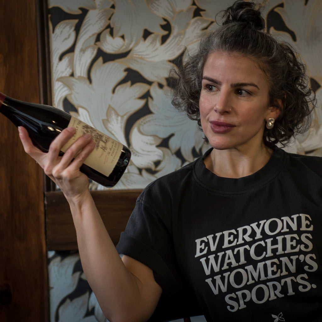 Woman holding a bottle of wine indoors with decorative wall in the background