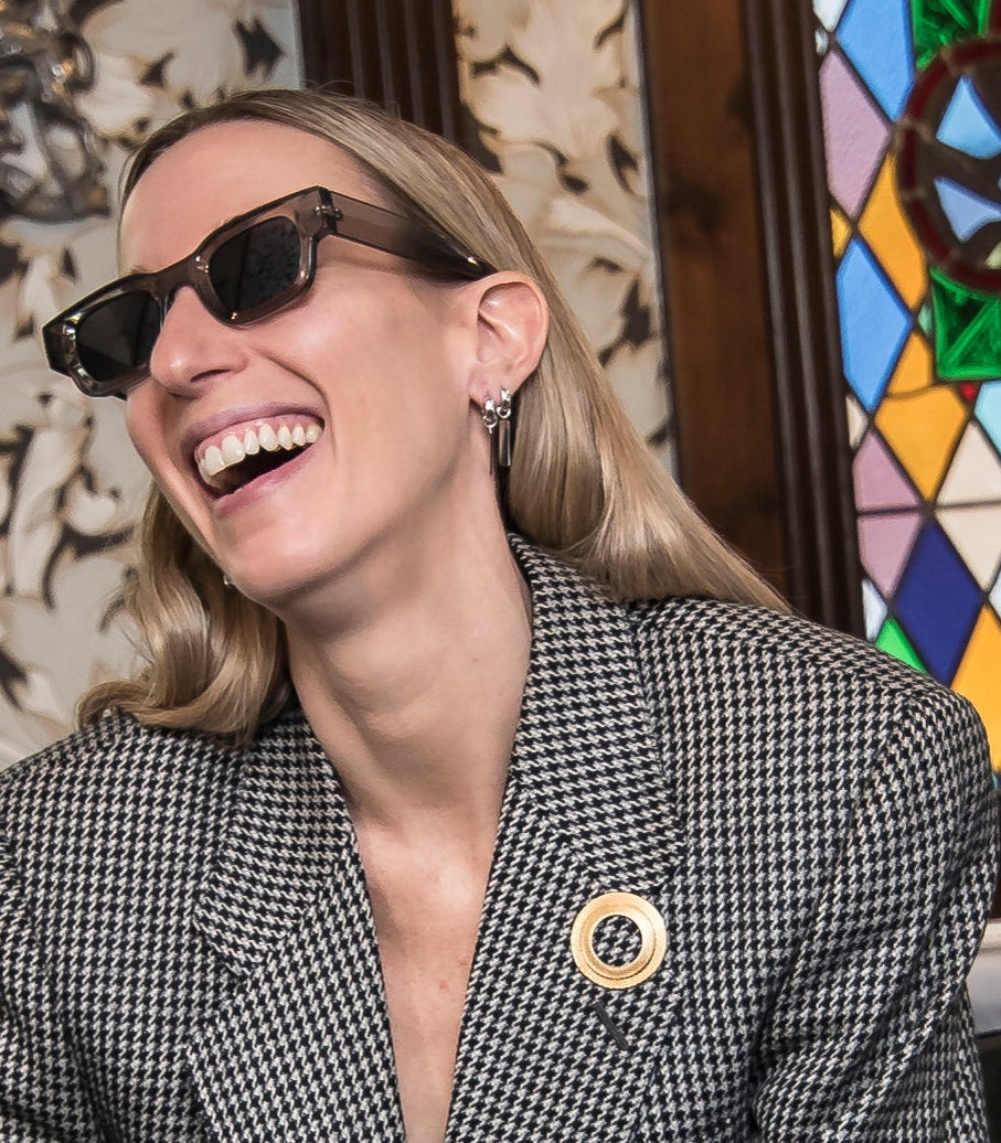 Woman wearing sunglasses and a patterned blazer in front of a stained glass window